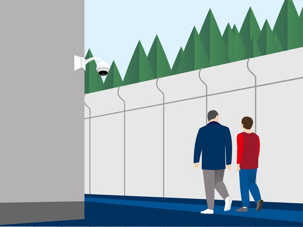Zwei Personen gehen entlang einer hohen Mauer Zwei Personen gehen entlang einer hohen Mauer
